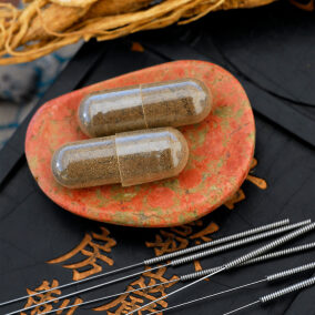 Herbal capsule, Ginseng root, and acupuncture needles.